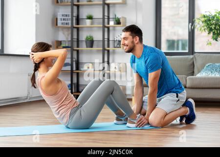 woman with personal trainer doing sit ups at home Stock Photo