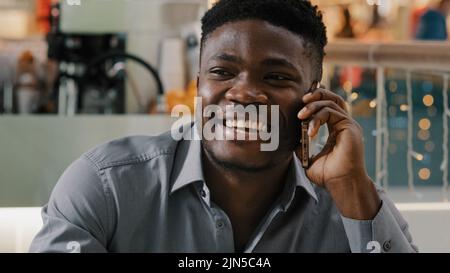 Close-up young happy african american man talking on phone answering friendly call making order in online store communicating on smartphone pleasant Stock Photo