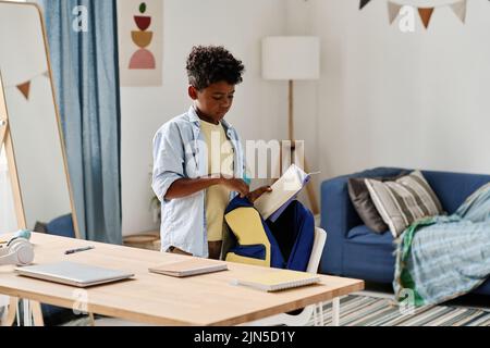 African schoolboy putting books in his backpack standing in his room, he preparing for school Stock Photo