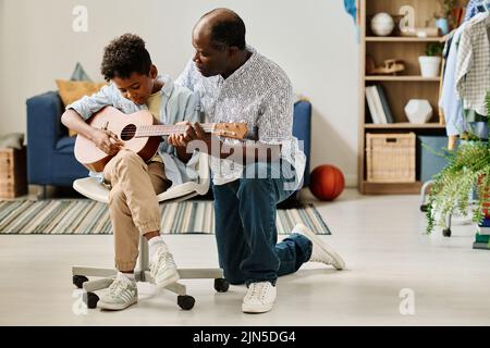 African teacher teaching his student to play guitar during home lesson in the room Stock Photo