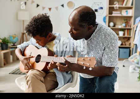 African boy having musical lesson with teacher at home, he teaching him to play guitar Stock Photo