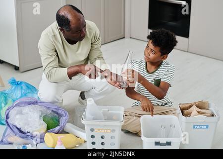 African father teaching his son to separate the rubbish in different containers in kitchen Stock Photo