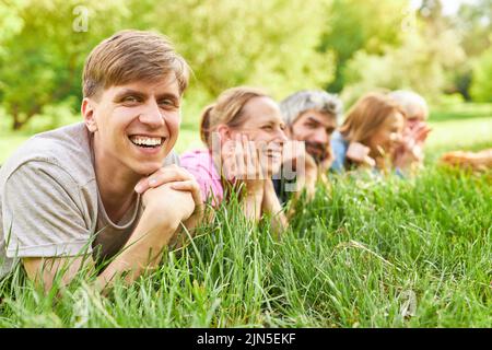 Laughing young man lying in the grass on a meadow in summer together with friends Stock Photo