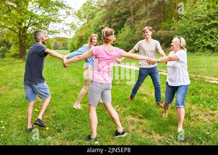 Young people standing in circle and holding hands at team building workshop in park Stock Photo