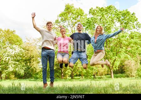 Four friends jump in the air together on a green meadow in summer Stock Photo