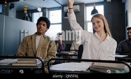 Diverse students classmates attentively listening to interesting lecture enthusiasm in classroom young caucasian girl raising hand knows answer Stock Photo