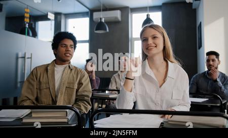 Diverse students classmates attentively listening to interesting lecture enthusiasm in classroom young caucasian girl raising hand knows answer Stock Photo