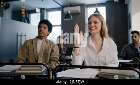 Diverse students classmates attentively listening to interesting lecture enthusiasm in classroom young caucasian girl raising hand knows answer Stock Photo