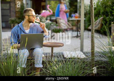 Man works on laptop while sitting at backyard Stock Photo