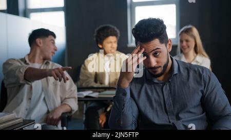 Young excited arab guy student sitting in classroom cannot concentrate on lesson being ridiculed by classmates suffering from abuse feeling distressed Stock Photo