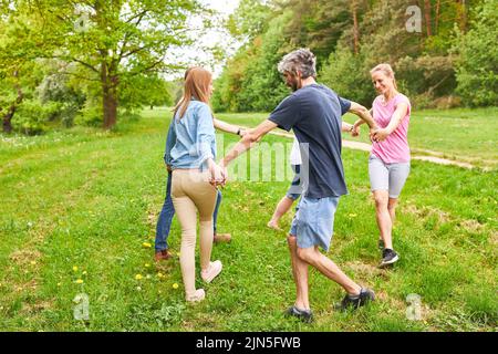 Young people doing exercise in team building workshop running in a circle on a meadow in the park Stock Photo