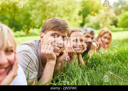 Smiling young man lying relaxed on a meadow with his friends Stock Photo