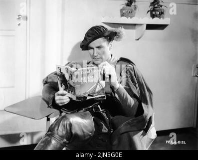 ERROL FLYNN in his Dressing Room holding his newly published book BEAM ENDS candid during filming of THE PRINCE AND THE PAUPER 1937 director WILLIAM KEIGHLEY novel Mark Twain music Erich Wolfgang Korngold costume Milo Anderson First National Pictures / Warner Bros. Stock Photo