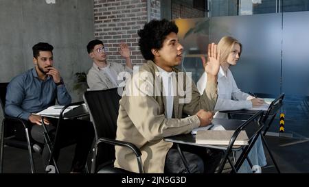 Diverse people sit in classroom at desk actively study science classmates students listen lecture seminar in college studying at school raise hands Stock Photo