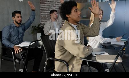 Students sit at desk in classroom at lesson young group people classmates listen to lecture at university or school raise hands knowing correct answer Stock Photo