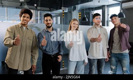 Happy professional confident group diverse people corporate employees standing in row looking at camera smiling showing thumbs up best appreciation Stock Photo