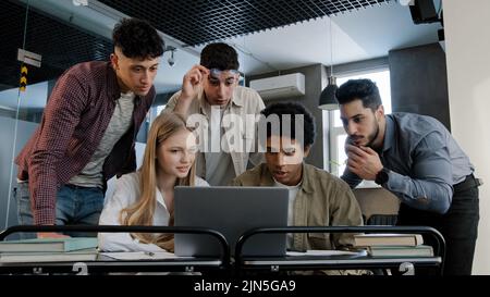 Focused diverse team corporate employees colleagues in office looking at laptop screen reading good news happy excited group workers celebrating Stock Photo