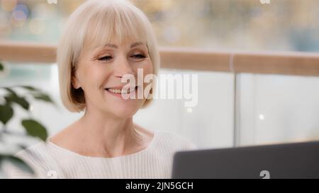 Close-up happy mature businesswoman typing on laptop working remote satisfied elderly woman communicates online with family using computer application Stock Photo