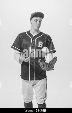 Portrait of young man, baseball player in uniform posing with ball and glove. Black and white photography Stock Photo
