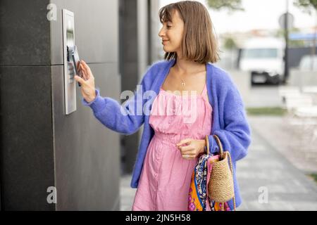 Young stylish woman getting access to the building by attaching smartphone to intercom Stock Photo