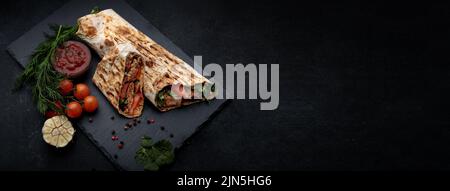 Shawarma with meat, cutaway, with sauce, tomatoes, cheese, herbs and garlic, on black slate, on a black background . Banner Stock Photo