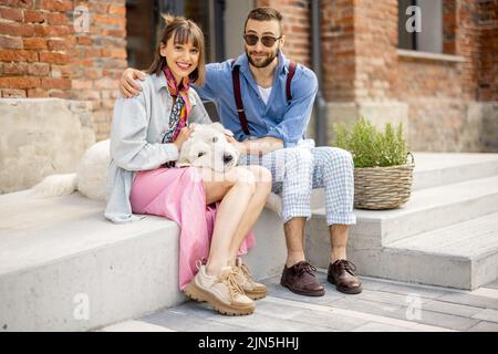 Stylish couple have fun and sit with their dog on a street Stock Photo