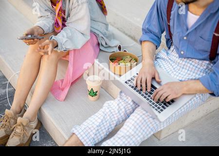 Stylish colleagues work on phone and laptop computer outdoors, close-up Stock Photo