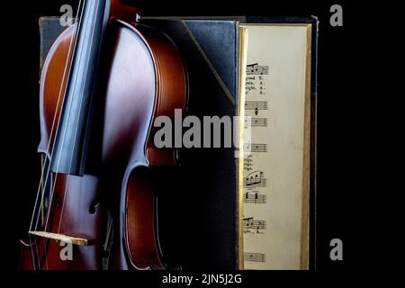 Upright violin against an old music book on a black background Stock Photo