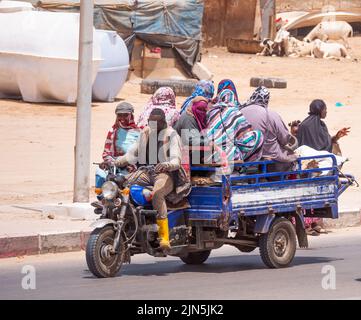 A threeweeler travel down a street carrying many people. The city is Nouakchott, Mauritania. Stock Photo