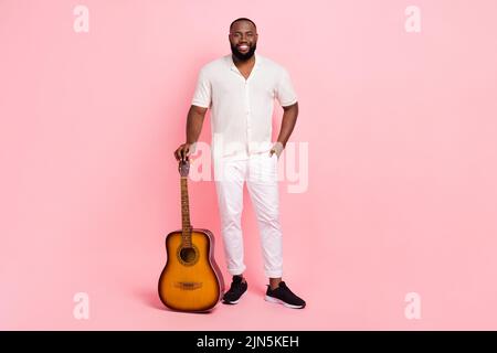 Photo of cute charming young man wear white shirt smiling holding acoustic guitar isolated pink color background Stock Photo
