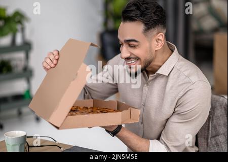 Happy man holding open pizza box indoors Stock Photo