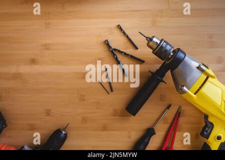 Flat lay view of drills with different drills and screwdrivers lying on a wooden table top. Stock Photo