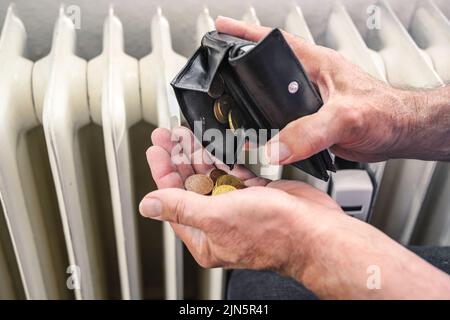 Hands of a man pouring out few coins from a wallet in front of an old heater, suffering from rising energy costs, copy space, selected focus, narrow d Stock Photo
