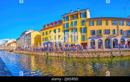 MILAN, ITALY - APRIL 9, 2022: The crowded embankment of Naviglio Grande Canal with old colorful houses and restaurants behind pedestrian alley, on Apr Stock Photo