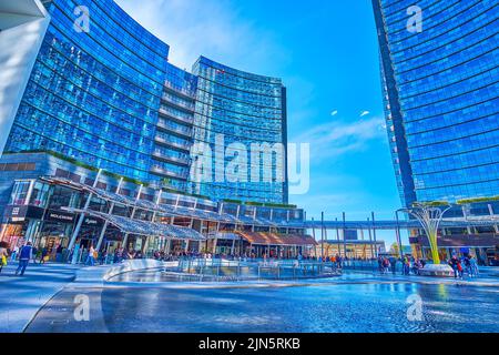 MILAN, ITALY - APRIL 9, 2022: Modern Piazza Gae Aulenti with its large pool is the most photogenic place for shopping and leisure strolls outside city Stock Photo