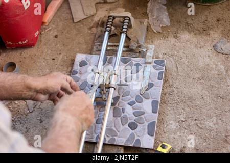 Builder uses tile cutter to cut floor tiles while finishing new home. Stock Photo