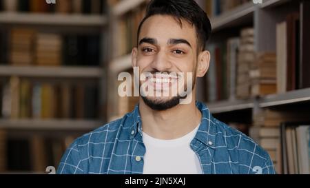 Close-up male portrait young handsome happy man standing in library looking at camera smiling healthy toothy smile waving nods head in approval Stock Photo