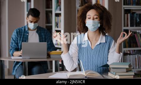 Tired female student sitting in library writing notes doing homework preparing for exam feel fatigue overworked stressful young woman in protective Stock Photo