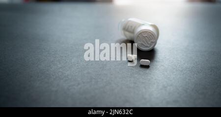 White tablets pills and blur child-resistant pill bottle on black table. Prescription drugs. Pharmaceutical industry. Medical care. Medication Stock Photo