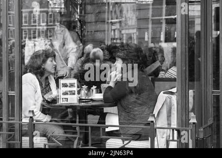 A cafe with reflections and two women seated at a table having a casual conversation and drinking tea, York, North Yorkshire, UK. Stock Photo