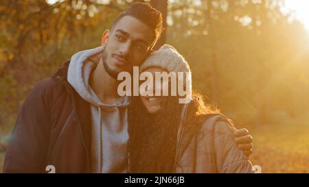 Young happy couple in love standing outdoors hugging admiring sunset in sunshine talking smiling laughing having fun together boyfriend and girlfriend Stock Photo