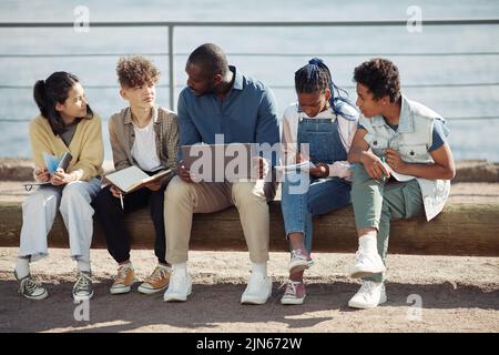 Full length shot of diverse group of kids with male teacher using laptop outdoors during Summer school lesson Stock Photo