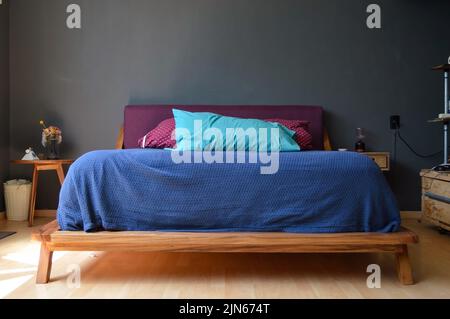 A cozy bedroom with an elegant blue and red bed and a wooden credenza on each side against the gray wall Stock Photo