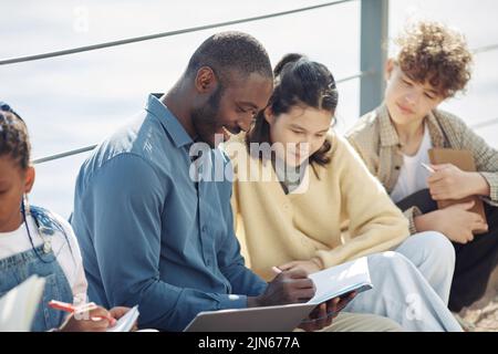 Side view portrait of smiling male teacher with diverse group of children during outdoor class Stock Photo
