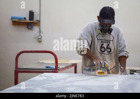 A professional woodworker using a woodworking sander on a piece of furniture in a factory Stock Photo