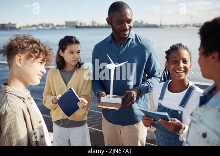 Portrait of black male teacher demonstrating wind mill model to group of kids during outdoor class in sunlight Stock Photo