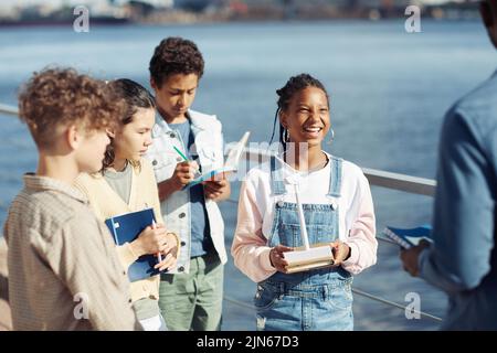 Diverse group of kids smiling happily while enjoying outdoor class in sunlight Stock Photo