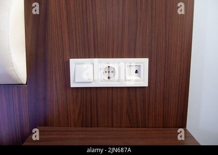 A close-up of white power socket, power outlet plug and light switch on a wooden panel wall. Stock Photo
