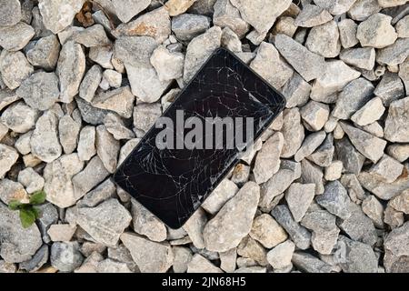 Black smartphone with broken display on the stones. Phone screen damage. Stock Photo