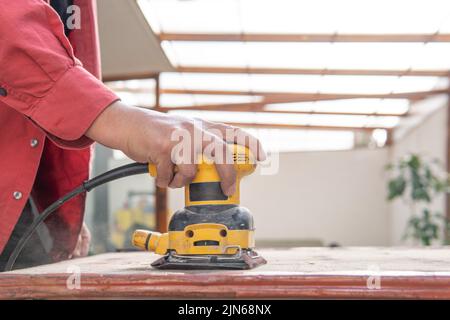 Hand of an unrecognizable man using a sander on a piece of wood. Carpentry and restoration concept Stock Photo